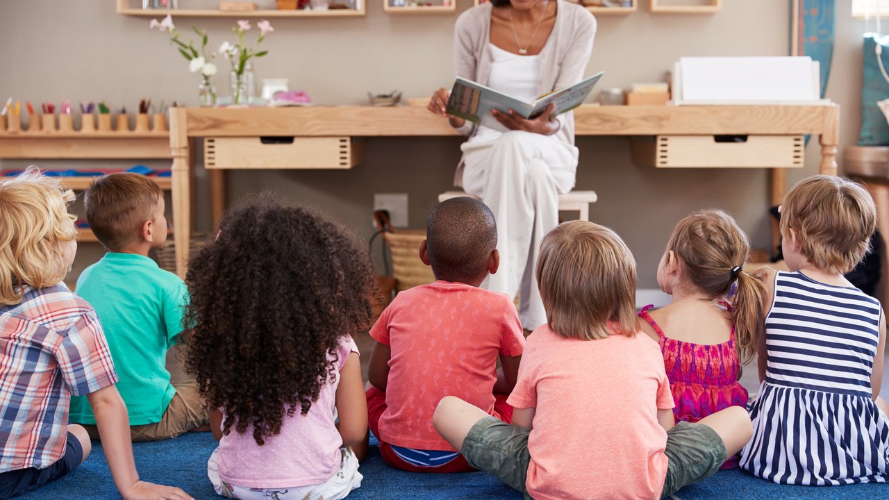 Kinder sitzen auf dem Boden vor einer Frau, die aus einem Buch vorliest