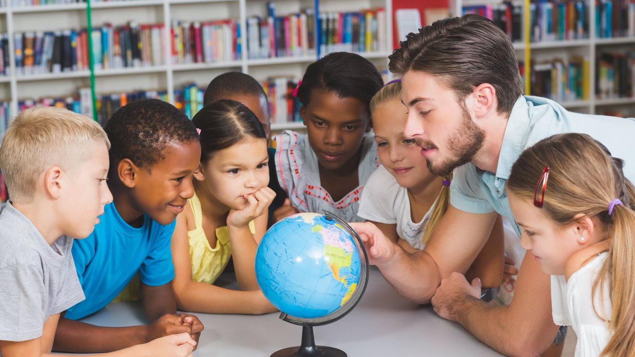 Ein Lehrer und mehrere Kinder sitzen um einen Globus