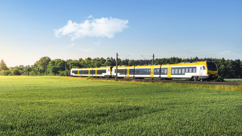 Eine neue Regionalbahn fährt hinter einer Wiese