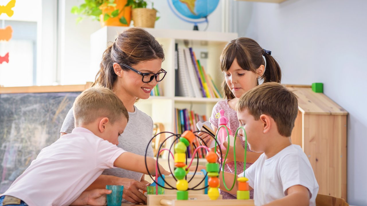 Eine Erzieherin sitzt mit drei Kindern an einem gemeinsamen Spiel. 