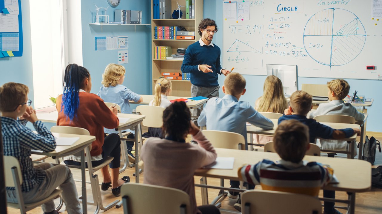Referat 74- Grund-, Haupt-, Werkreal-, Real-, Gemeinschaftsschulen und Sonderpädagogische Bildungs- und Beratungszentren Ein Lehrer erklärt den Schüler:innen und Schüler einer Grundschule Mathematik