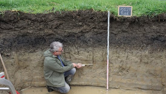 Mann steht in einer Grube und misst mit einem Zollstock die Erdschichten
