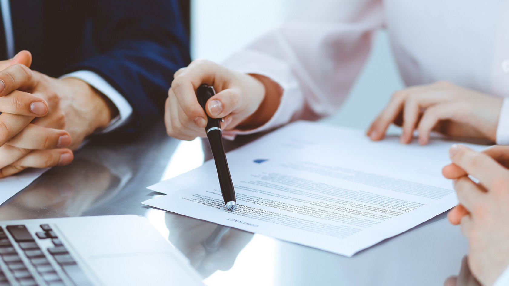 Drei Personen sitzen am Tisch um ein Dokument und einen Laptop