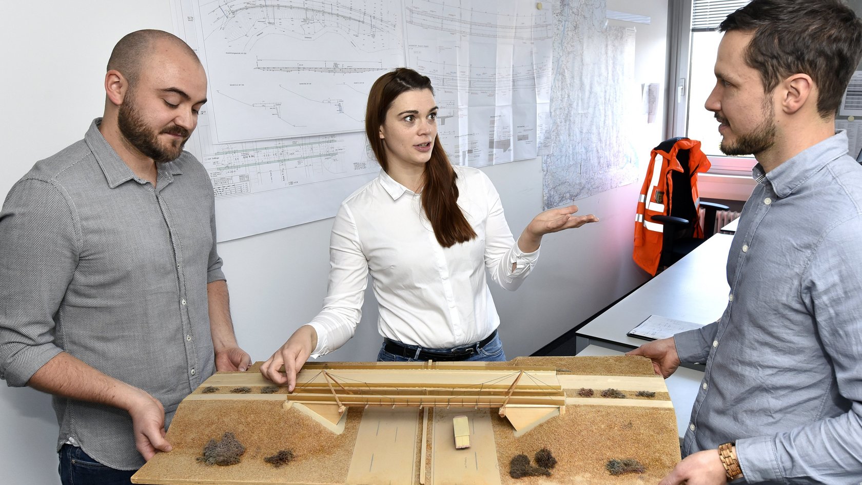 Zwei Männer und eine Frau halten eine Brückenvisualisierung (3D) in den Händen