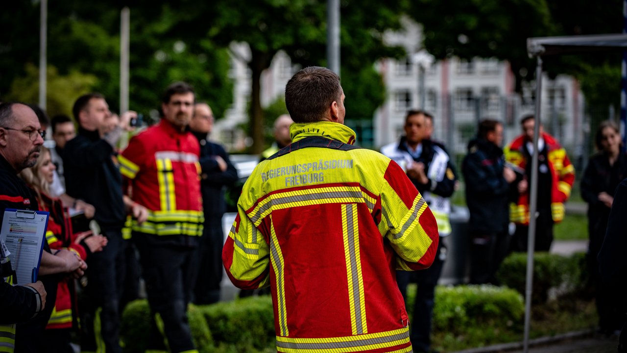 Referat 16 - Polizeirecht, Feuerwehr, Katastrophenschutz, Rettungsdienst Mann in Jacke des Regierungspräsidiums steht vor Einsatzkräften in einem Kreis