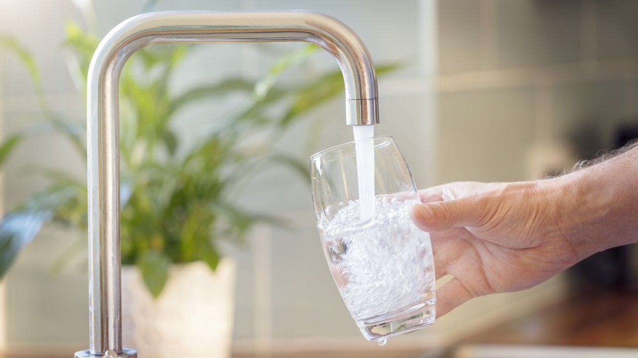 Ein Glas wird unter einen laufenden Wasserhahn gehalten
