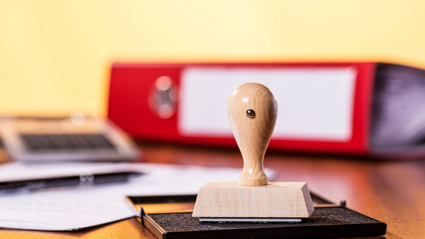 Stempelkissen mit Stempel und rotem Ordner im Hintergrund