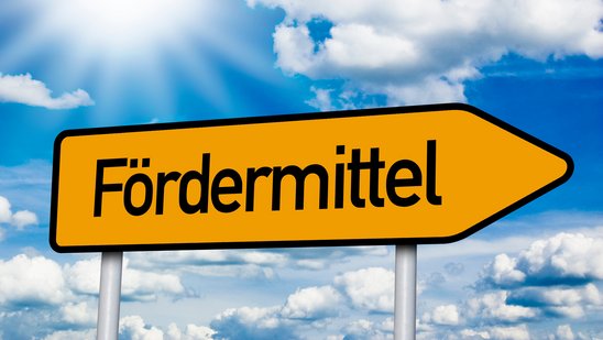 Gelber Pfeil. Schwarze Schrift Fördermittel. Bildhintergrund blauer Himmel mit weißen Wolken.