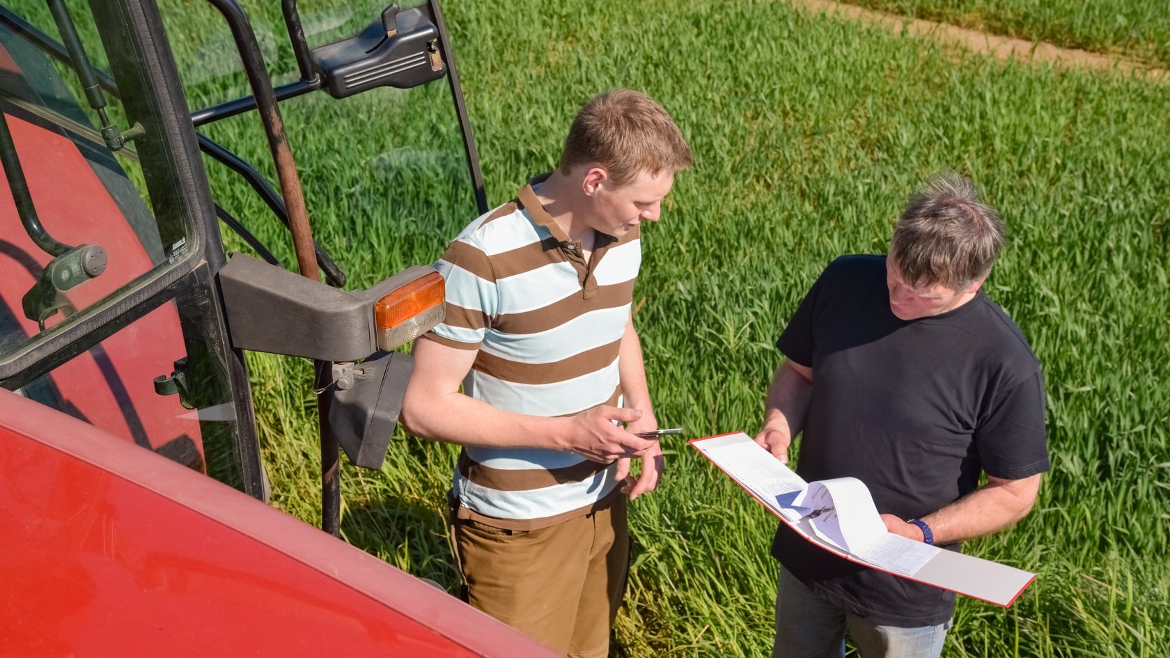 Ein Landwirt und ein Prüfer vor einem Feld und neben einem Traktor im Gespräch