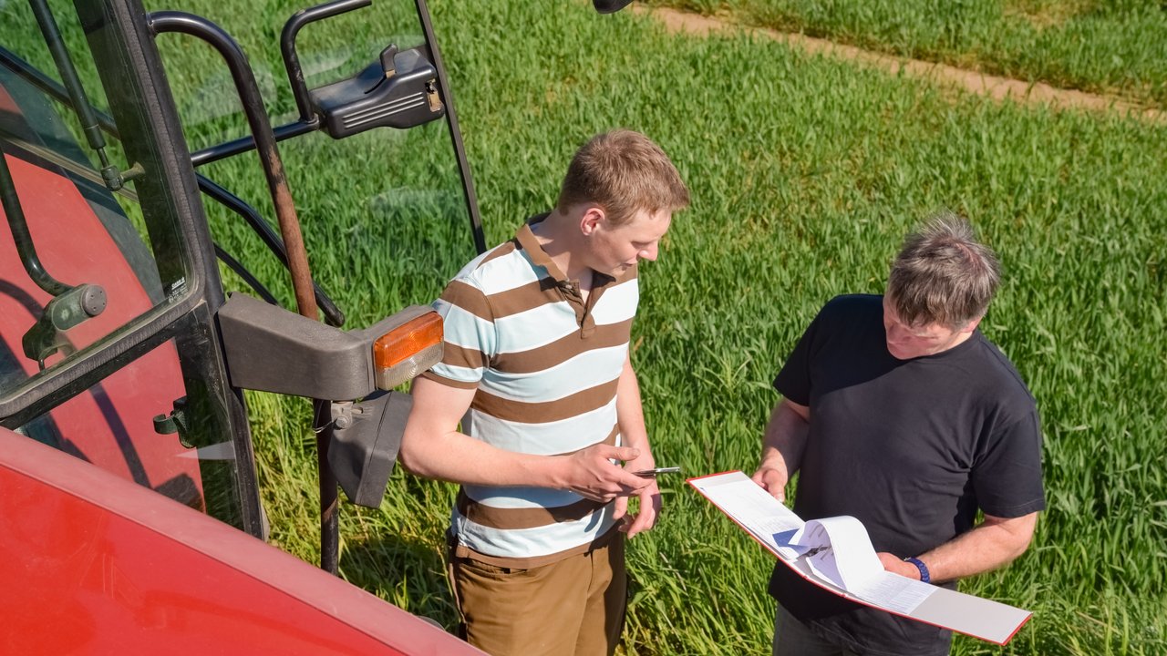 Zwei Personen stehen neben einem Traktor vor einem Feld
