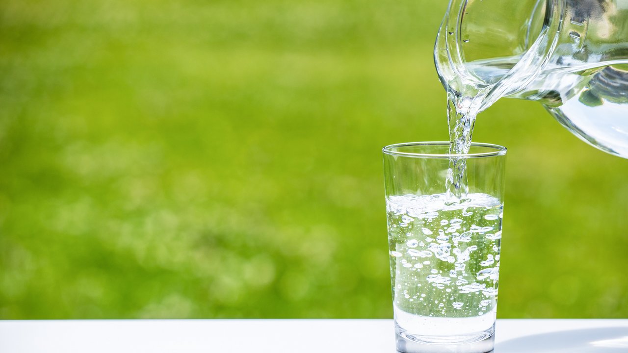 Aus einer Karaffe Wasser wird Wasser in ein Wasserglas gefüllt