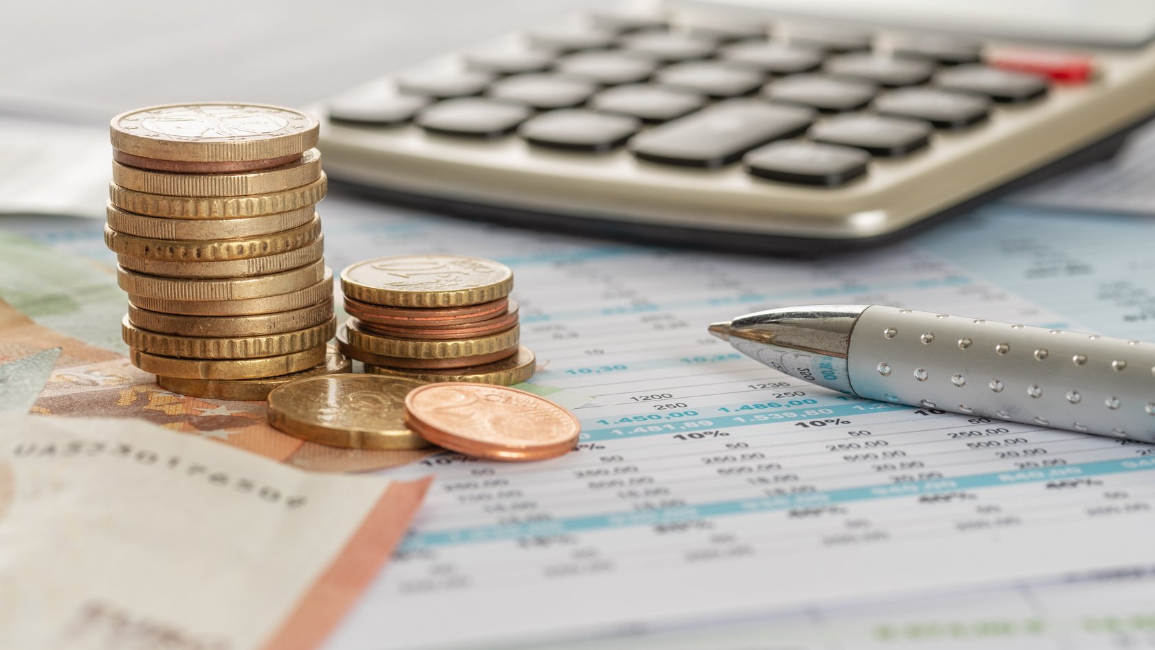 Geld und ein Taschenrechner liegen zusammen mit einem Kulli auf einem Tisch