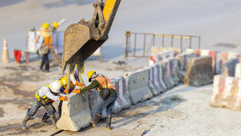 Bauarbeiter an einem Betonstück mit Überstützung eines Baggers