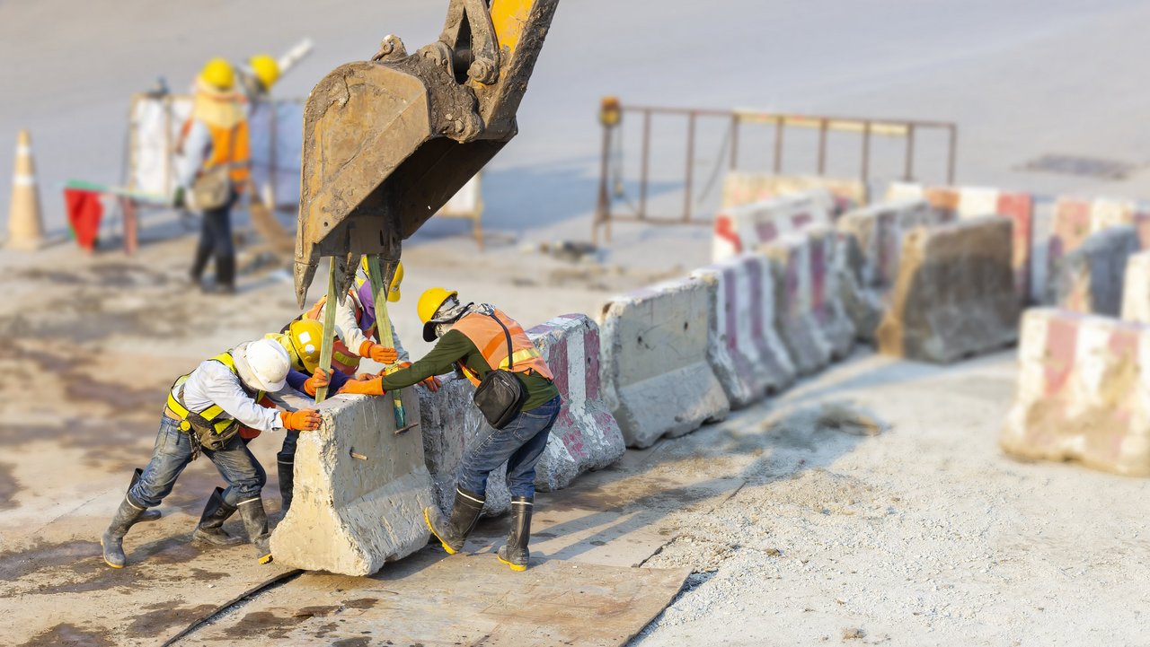 Bauarbeiter an einem Betonstück mit Überstützung eines Baggers