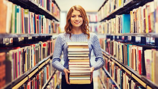 Eine Frau hält einen Bücherstapel zwischen zwei Bücherregalen