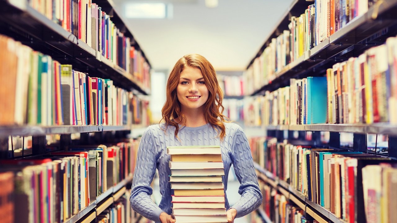 Eine Frau hält einen Bücherstapel zwischen zwei Bücherregalen
