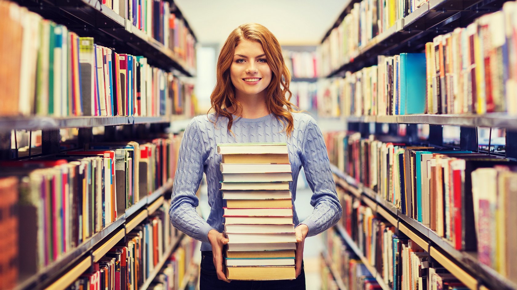 Eine Frau hält einen Bücherstapel zwischen zwei Bücherregalen