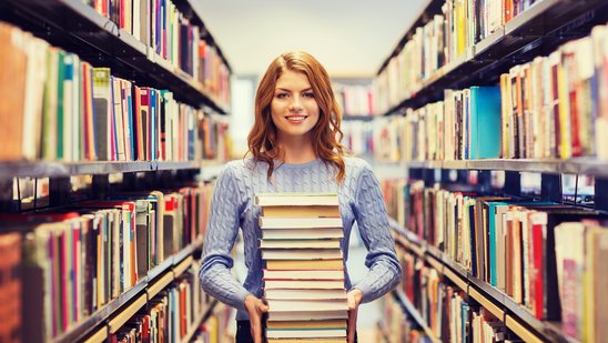 Eine Frau hält einen Bücherstapel zwischen zwei Bücherregalen