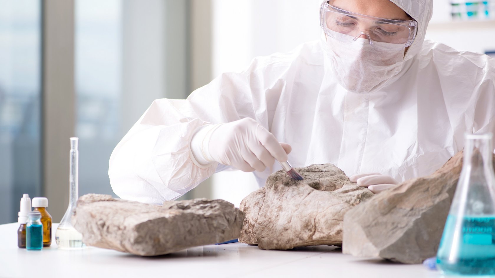 Eine Frau in Schutzkleidung untersucht Gesteinsarten im Labor