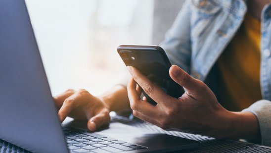 Ein Mann sitzt mit Handy vor einem Laptop