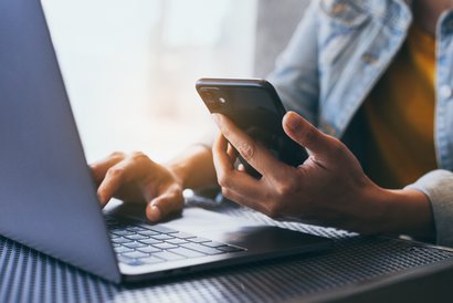 Ein Mann sitzt mit Handy vor einem Laptop