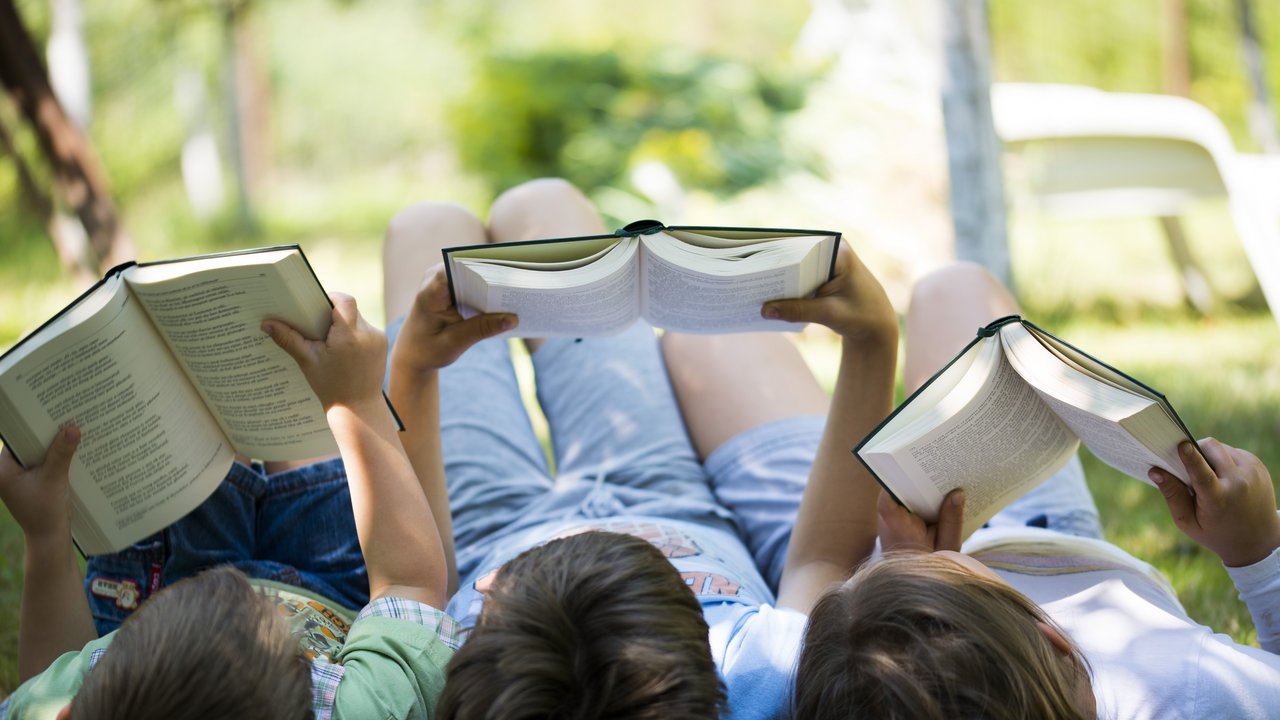 Drei Kinder liegen im Gras und lesen