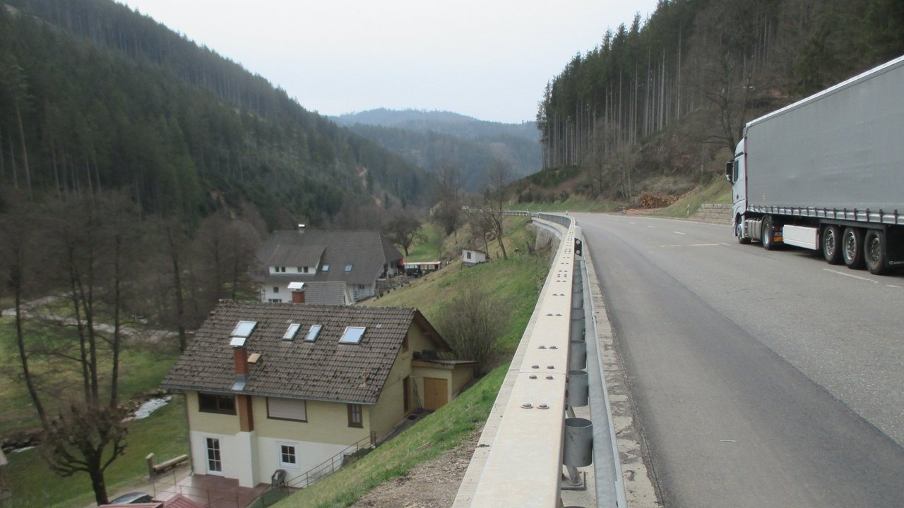 Ein LKW fährt über eine Straße bei Triberg, man sieht links im Bild ein Haus an einem Hang mit Stützmauer